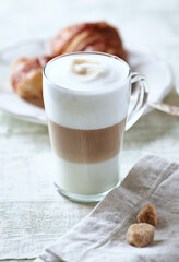Glass of Latte Macchiato with Croissant. Bright wooden background. Close up.