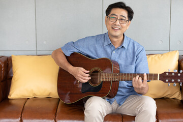 portrait senior asian man playing guitar at home