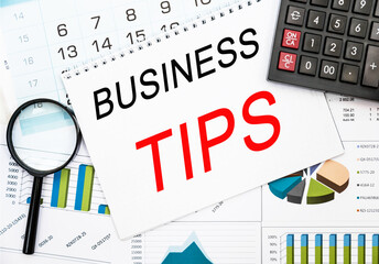 Text BUSINESS TIPS on financial tables with magnifying glass. Business and financial conzept. calculator, magnifying glass and the working paper with a diagram.