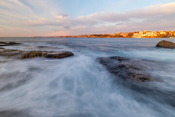 Rocky coastline with sea water flowing under the cloudy sky.
