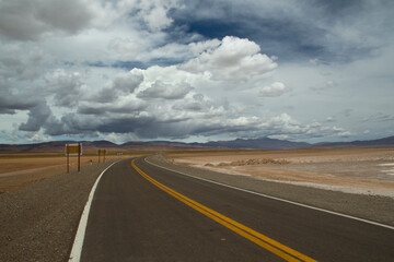 Empty road curve. Traveling along the asphalt highway across the arid desert under a dramatic sky with beautiful clouds. 