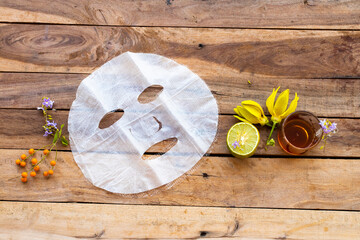 natural aroma sheet mask extract honey, lemon herbal vegetation  health care for skin face essence face mask and flower ylang ylang arrangement flat lay style on background wooden