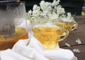 Cups of tea with chamomile flowers and teapot on wooden background