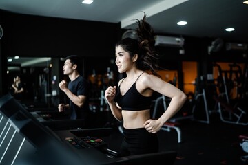 Fototapeta na wymiar An attractive Asian woman wearing a black sportbar is exercising on a treadmill in a fitness gym.