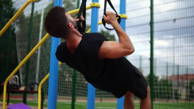 Muscular sportsman doing hanging pull ups exercise using fit belt to force strenth of workout outdoors