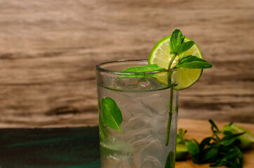 Mojito, cóctel de origen cubano, sobre mesa verde decorada con ingredientes del cóctel. Fondo de madera.