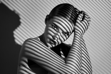 Black and white portrait of a beautiful woman with a shadow pattern on the face and body in the form of stripes.