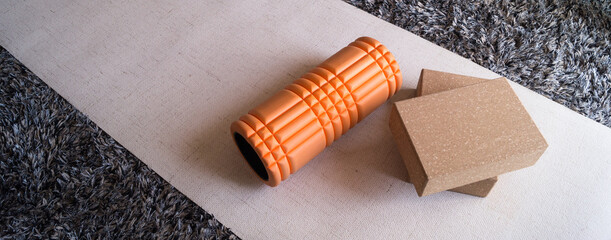Orange foam roller and two yoga blocks on a beige mat