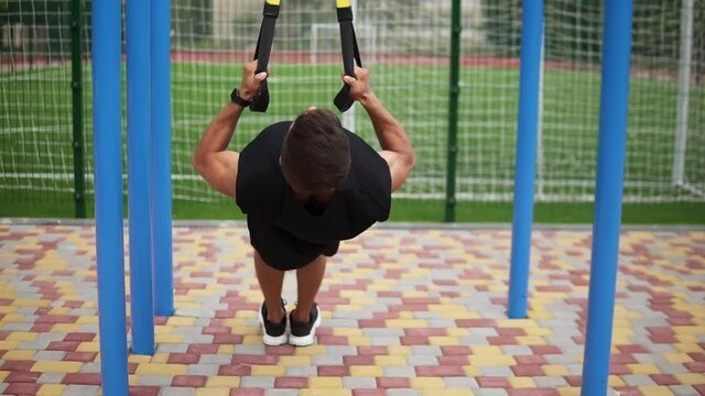 Caucasian sportsman doing pull ups exercise using fit belt to force strenth of workout outdoors