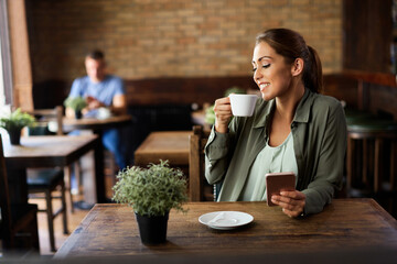 Happy woman enjoying in cup of coffee while using smart phone in a cafe,
