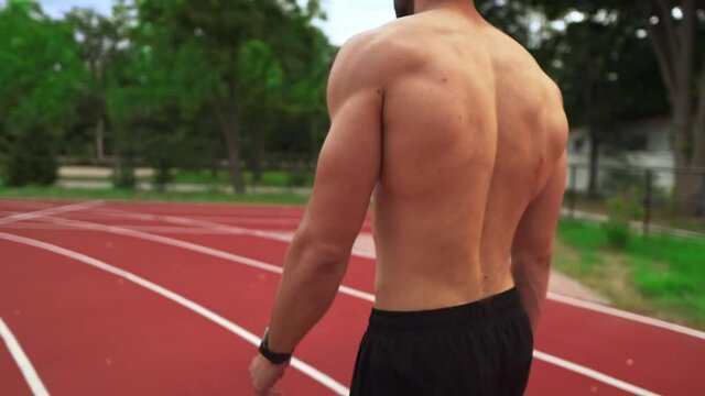 Tired, shirtless man going on stadium race after hard training