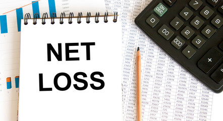 The inscription on the tablet with a fixed sheet of paper NET LOSS, next calculator, graphs, reports.