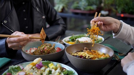 Two people with chopsticks enjoying their bowls full of healthy meals in Asian cuisine style Dinner...