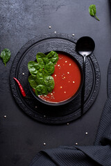 tomato puree soup with spinach in a black bowl, top view