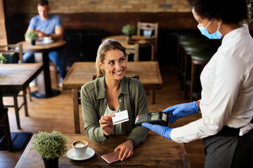 Happy woman making contactless payment in a cafe during coronavirus epidemic.