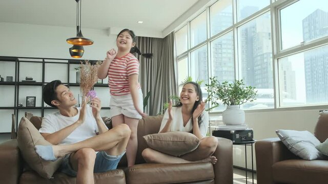 4k joyful pleasure in quarantine period happiness asian family mom dad daughter enjoy singing together on sofa couch in living room fun activity social distancing new normal lifestyle