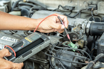Fototapeta premium A car mechanic uses a meter to measure the electricity in the engine in front of the car