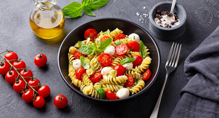 Pasta fusilli with mozzarella cheese, tomatoes and basil. Grey background. Close up.