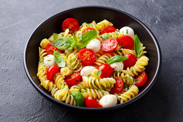 Pasta fusilli with mozzarella cheese, tomatoes and basil. Grey background. Close up.