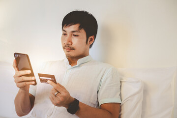 A handsome man is holding credit card and using a mobile phone shopping online. The busines is working at home. Online shopping, e-commerce, internet banking, spending money, working from home concept