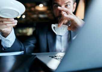 Business man sitting in a cafe with a cup of coffee in his hands in front of a laptop technology communication
