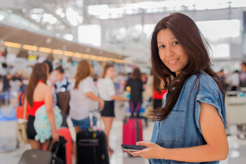 Asian woman using mobile phone with feeling happy and smiley face, check flight at the international airport to travel on weekends in airport terminal.
