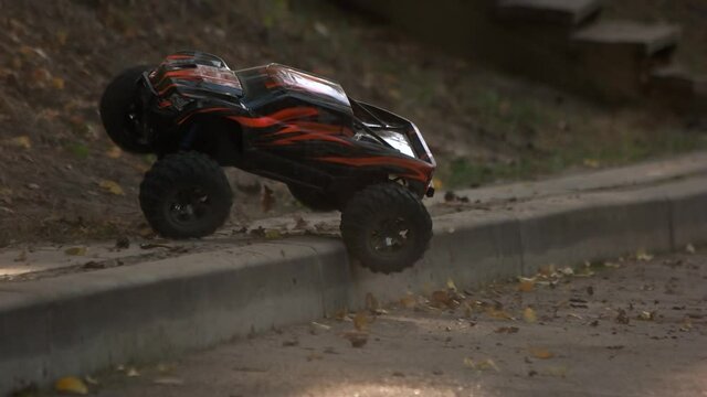 Remote control monster car crossing road curb. Toy rc car rides off the road.