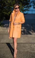 Fototapeta premium Woman in orange coat at street, woman outfit. Fancy style for ladies, autumn colors and fashion 