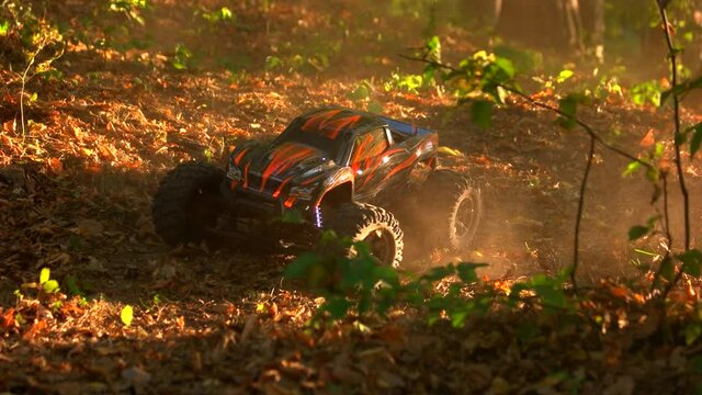Monster truck rc car rides over dried autumn leaves. Remote controlled miniature car model on offroad forest race.