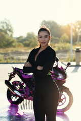 Fototapeta na wymiar Seductive young woman in tight fitting black suit poses near sport motorcycle at self service car wash.