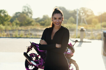 Beautiful young woman in tight fitting black suit poses near sport motorcycle at self service car wash.