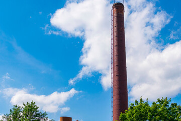 Brick chimney of a city boiler house on a background of blue sky.