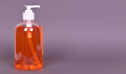 A bottle of orange liquid soap on a grey background.