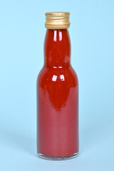 Hot red chilly sauce in little glass bottle on blue background.