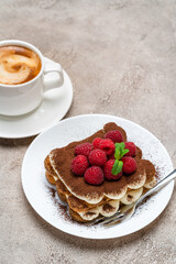 portion of Classic tiramisu dessert with raspberries and cup of coffee on grey concrete background