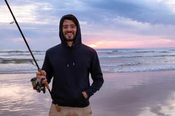 A young man fishing in the open sea along the Atlantic Ocean shoreline at Costa da Caparica in...