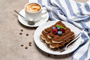 portion of Classic tiramisu dessert with raspberries, bluebedrries and cup of coffee on grey concrete background