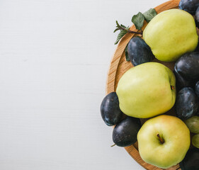 Top view of plums and apples in the wooden plate on white background.