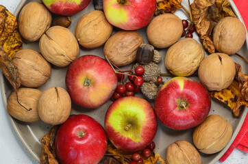 autumn decor walnuts apples rowan branch acorns on ceramic plate top view, autumn food concept