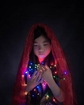 Teenage girl holding colorful illuminated Christmas lights while sitting indoors
