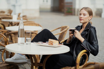 Waiting for a friend in a summer cafe, portrait of a young woman of European appearance ordered Breakfast, a Cup of cappuccino and delicious sugar desserts cake. 