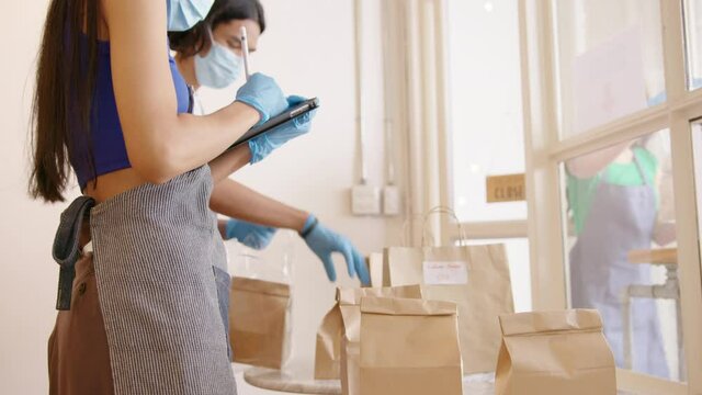 Online store, shop, restaurant or cafe preparing food take out paper bag for delivery service wearing protection gloves mask packing product ready for pick up in Small business during covid concept.