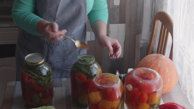 adult woman prepares glass jars with tomatoes and cucumbers for canning with special tool  and adds brine and vinegar
