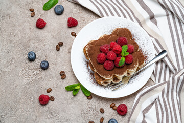 portion of Classic tiramisu dessert with raspberries and blueberries on grey concrete background