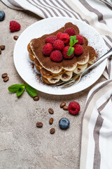portion of Classic tiramisu dessert with raspberries and blueberries on grey concrete background