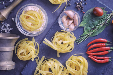 Pasta on the table with spices and vegetables. Noodles with vegetables for cooking on a black stone background.