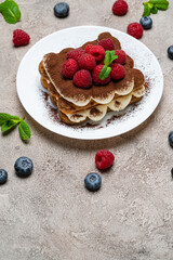 portion of Classic tiramisu dessert with raspberries and blueberries on grey concrete background
