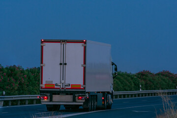 Truck with refrigerated semi-trailer seen from behind on the highway at dusk.