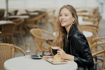 confident young blonde woman. drinks hot flavored delicious cappuccino coffee in a paper Cup. He looks at his friend and smiles. I made an order at a summer cafe