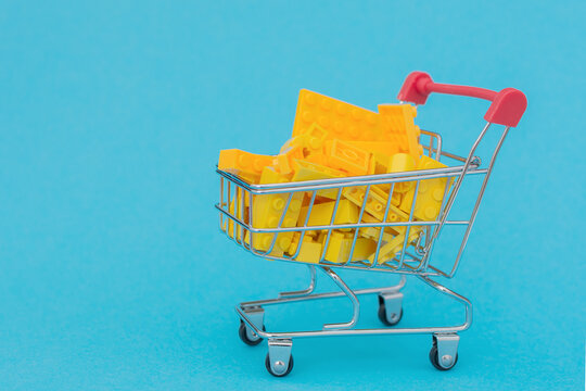 there are many small yellow blocks of different shapes in the basket. Trolley on a blue background, color contrast. Close-up. Concept - delivery, purchase, online store, construction.